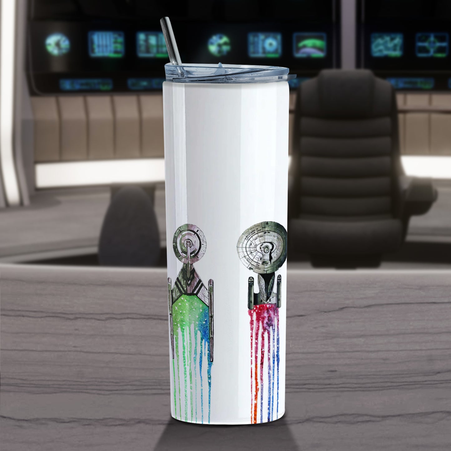 A white travel mug on a grey ledge. On the surface of the mug are images of spaceships from Star Trek, with small segments of deep space behind each. At the top of the mug is a stainless steel straw. Behind the mug is the bridge of a Star Trek ship.
