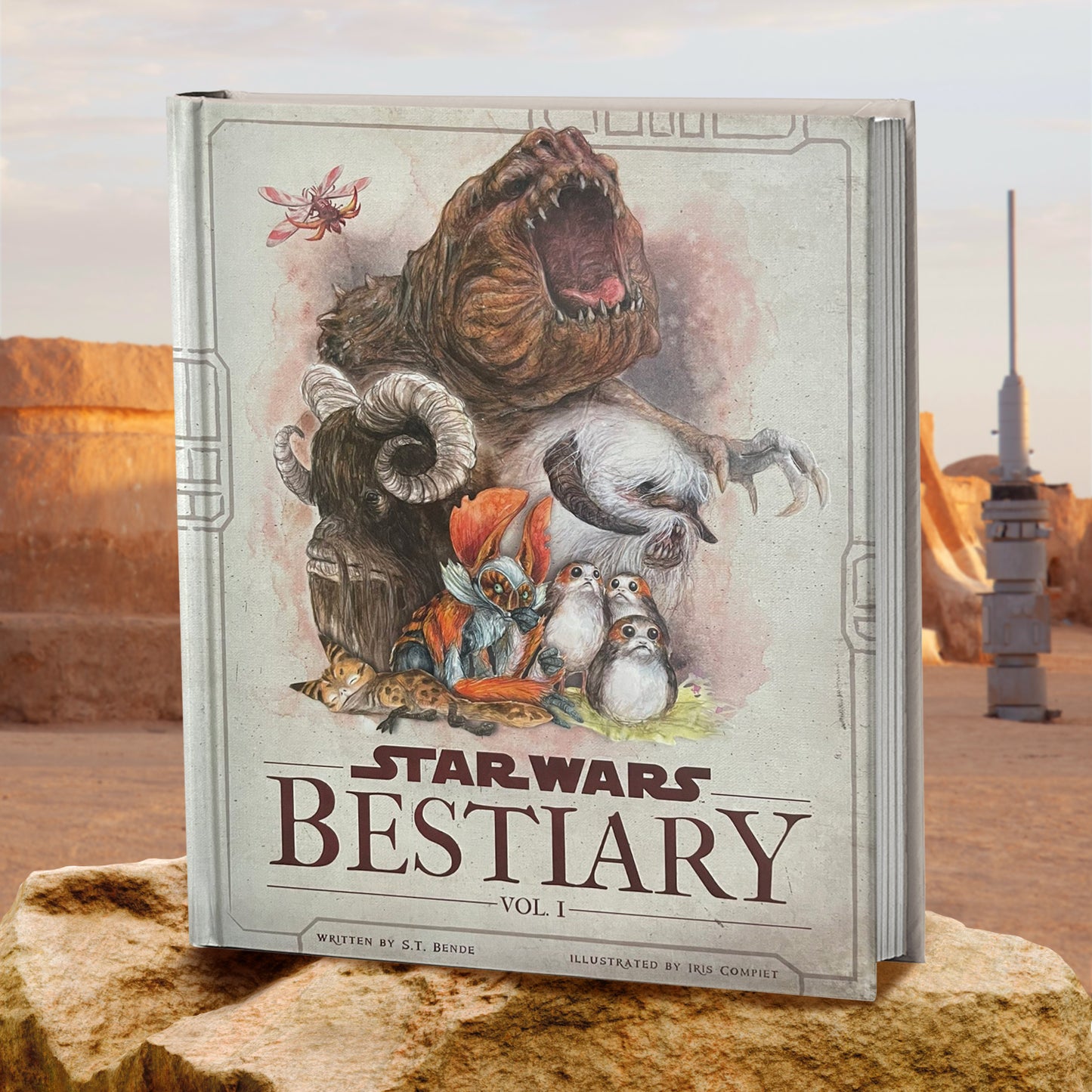 A hardcover book standing on a stone in the desert. On the cover are drawings of creatures from the Star Wars universe. Dark brown text at the bottom says "Star Wars Bestiary Volume 1." In the background is the Tatooine desert with a moisture vaporator in the ground.