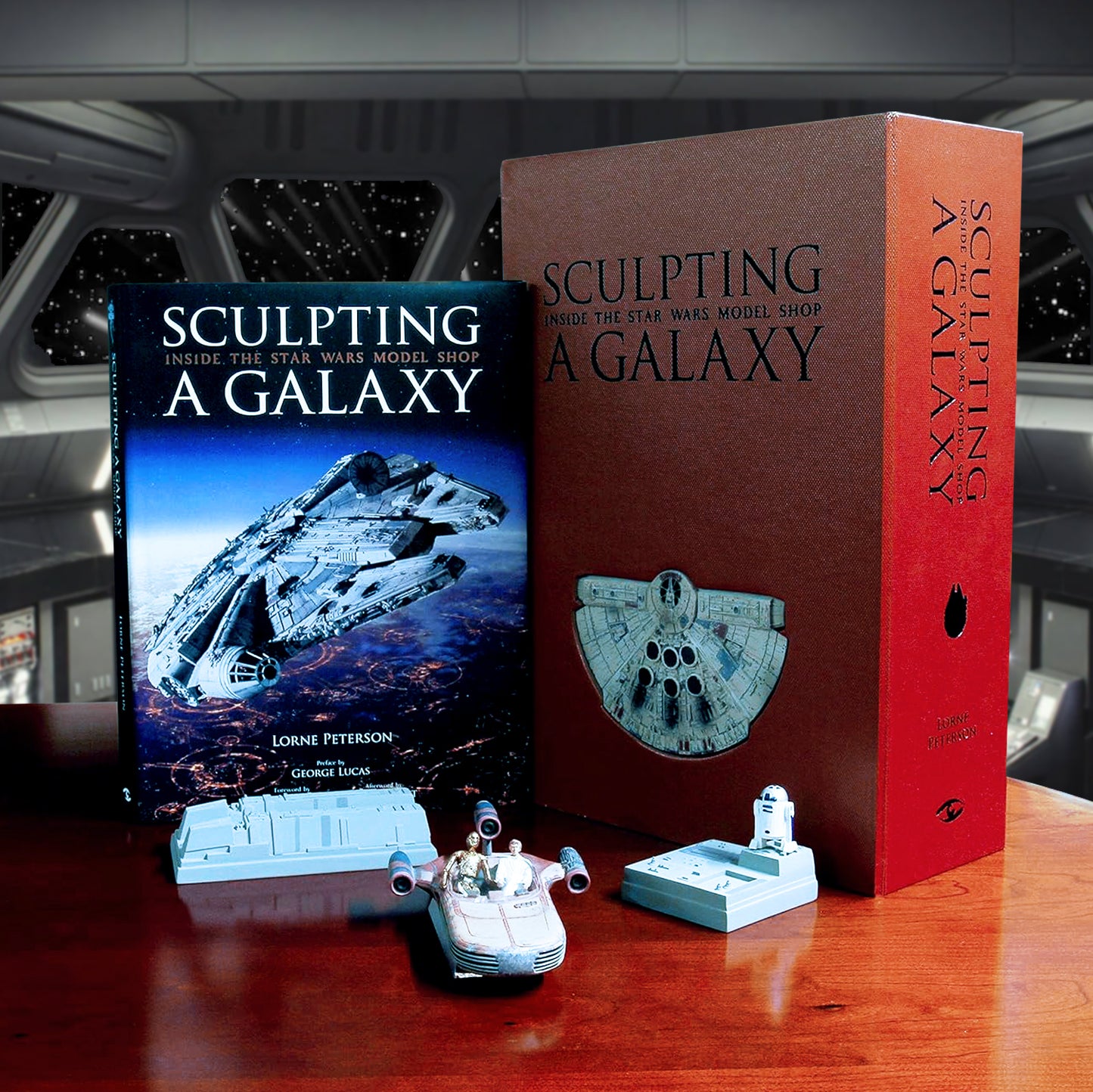 A brown box on a wood table. Across the top is black text that says "Sculpting A Galaxy: Inside the Star Wars model Shop." In the foreground is an open box with a Star Wars landspeeder miniature, model pieces for the Millennium Falcon, and a softcover book with Star Wars ships on the cover. In the background is is the bridge of a Star Wars spaceship.