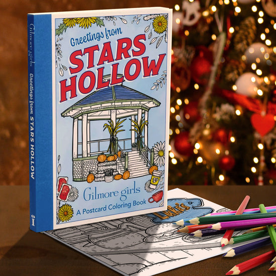Coloring book titled 'Greetings from Stars Hollow' by Gilmore Girls with coloring paper and pencils against a Christmas background.