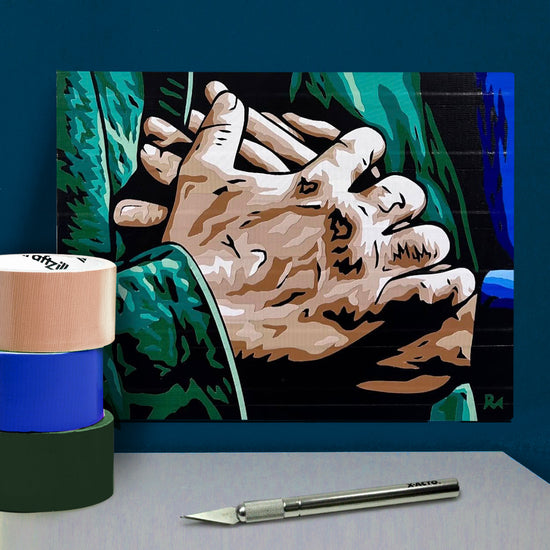 A poster made of layered pieces of duct tape, depicting the clasped hands of Sam and Dean Winchester. In front of the poster is an X-acto knife and rolls of duct tape.