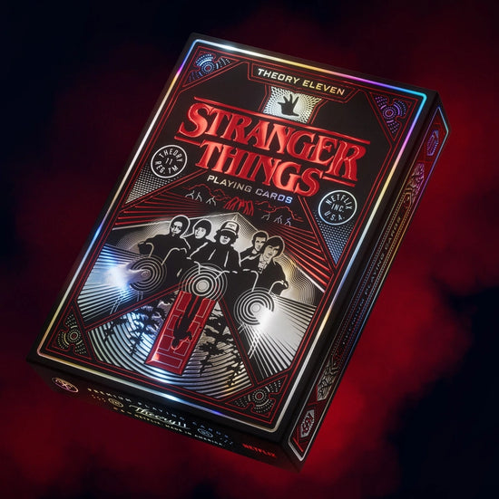 A red and black box of playing cards against a smoky red background. The box depicts characters and images from the TV series "Stranger Things."