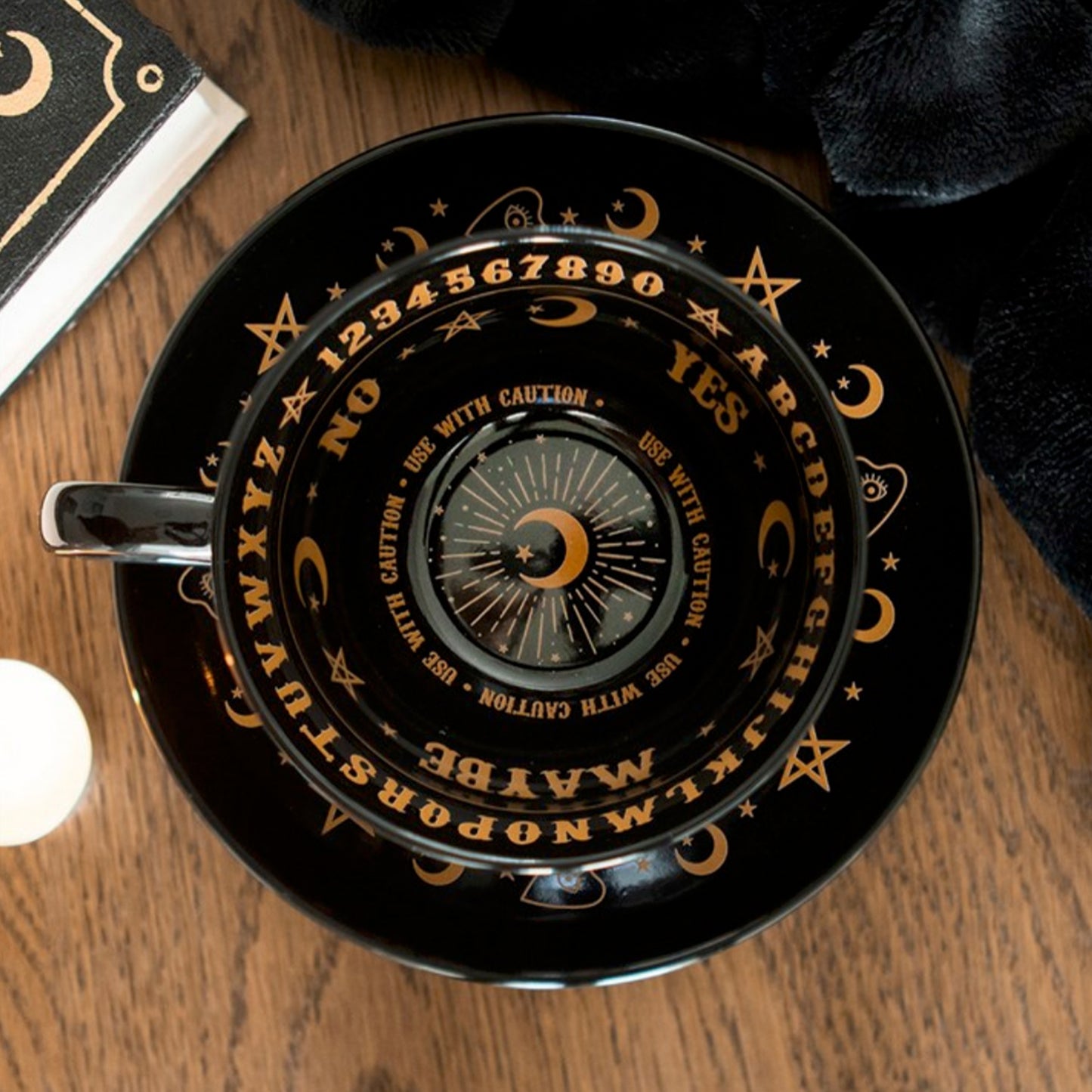 Black tea cup with gold lettering and symbols on a wooden surface