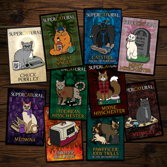 A collection of enamel pins on a wooden table. Each pin depicts a character from the TV series "Supernatural" reimagined as cats