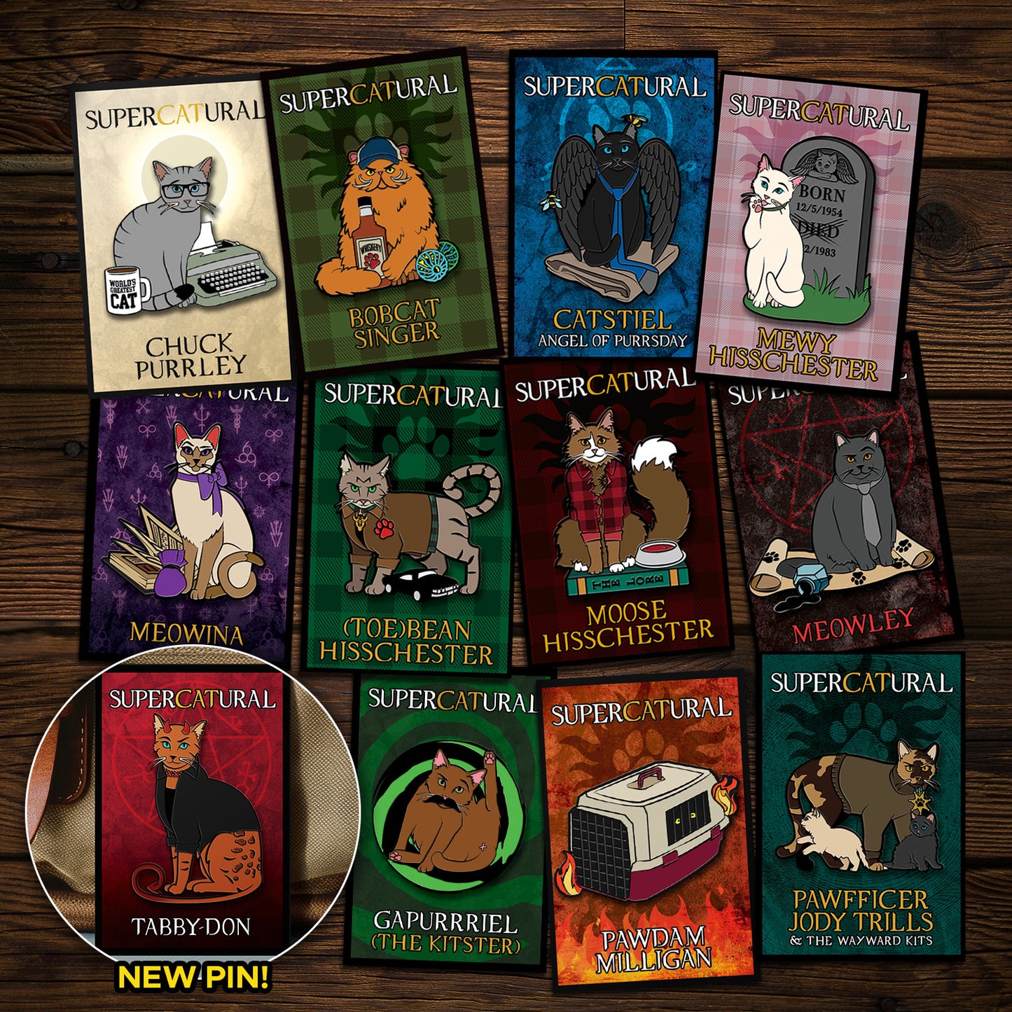 A collection of enamel pins on a wooden table. Each pin depicts a character from the TV series "Supernatural" reimagined as cats. An inset in the bottom left corner reads "NEW PIN!" and has an image of Tabbydon, the newest pin.