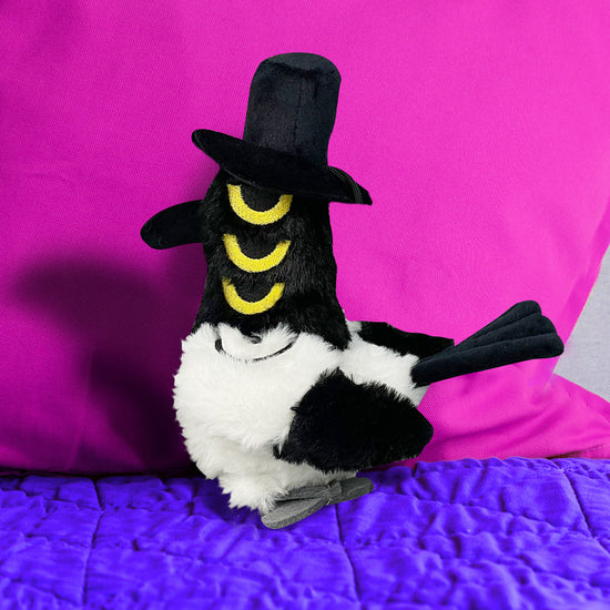 Plush toy resembling a black and white creature with yellow accents on a purple surface.