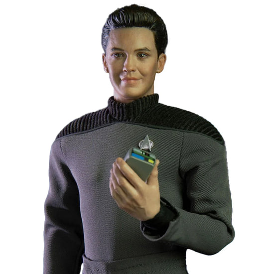 An action figure depicting the character Wesley Crusher from the TV series "Star Trek: The Next Generation." The figuring is dressed in Wesley's iconic grey uniform, and is against a white background. In the figure's left hand is a tricorder from the series.