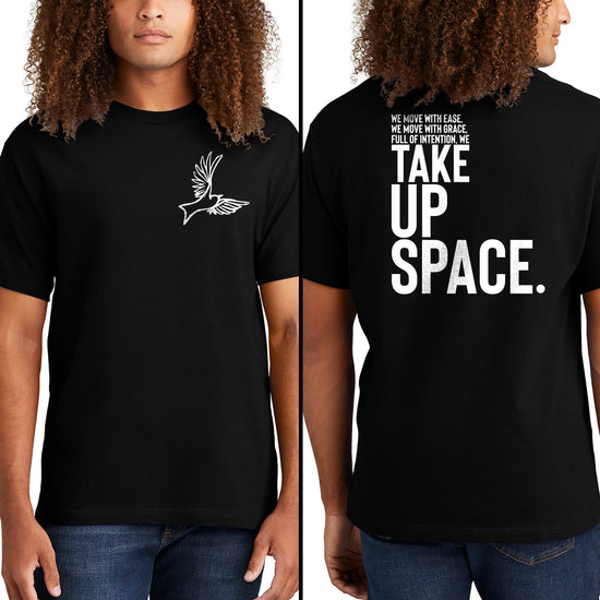 An image of a male model on a white background, wearing a black t-shirt. On the front of the shirt is a white drawing of a dove. On the back in white text is "We move with ease, we move with grace, full of intention, we take up space."