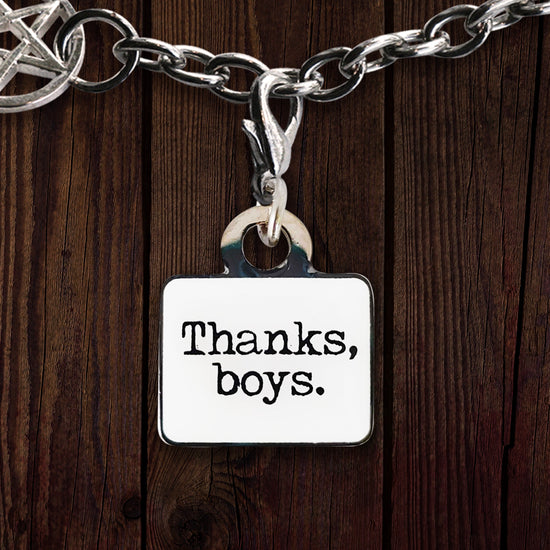 A white charm against a wooden background. The charm depicts an FBI badge, with Sam Winchester's face at the side. At the bottom is white text saying "Special agent James Page."