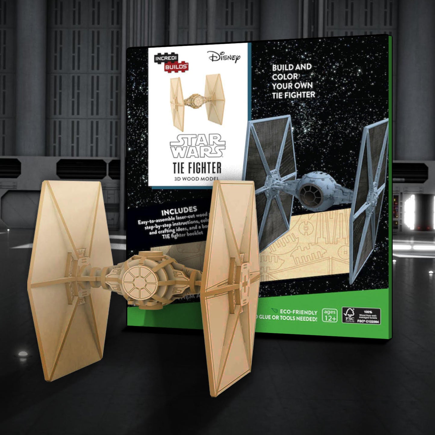 A box depicting a TIE Fighter from the Star Wars movies. The box is sitting against a dark grey starship background and depcits a wood model version next to it. Below the ship is a wood sheet with the model parts to be assembled. In front of the box is an assembled and unpainted TIE fighter model.