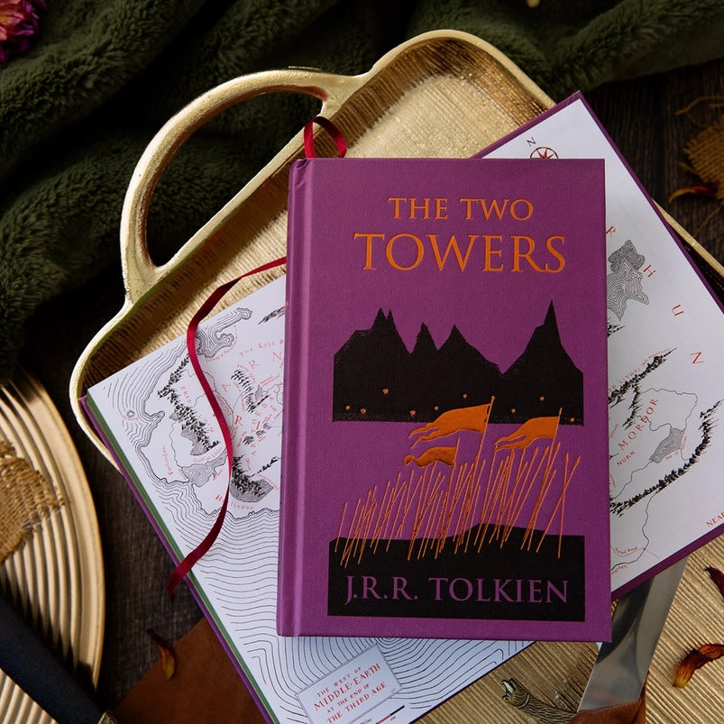 Two purple hardcover books on a wooden tray. The front cover of one book depicts a minimalist drawing of orange war flags against black mountains. Orange text says "The Two Towers." The second book is open to show a drawing of a map depicting Middle Earth.