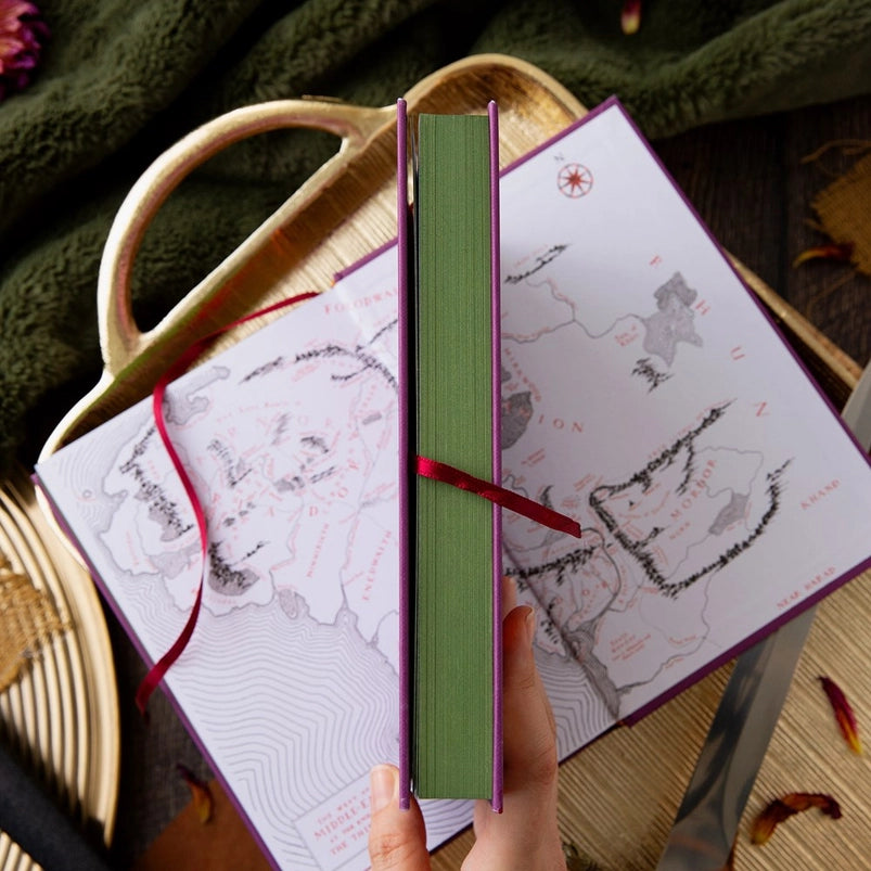 Two purple hardcover books on a wooden tray. The front cover of one book depicts a minimalist drawing of orange war flags against black mountains. Orange text says "The Two Towers." The second book is open to show a drawing of a map depicting Middle Earth.