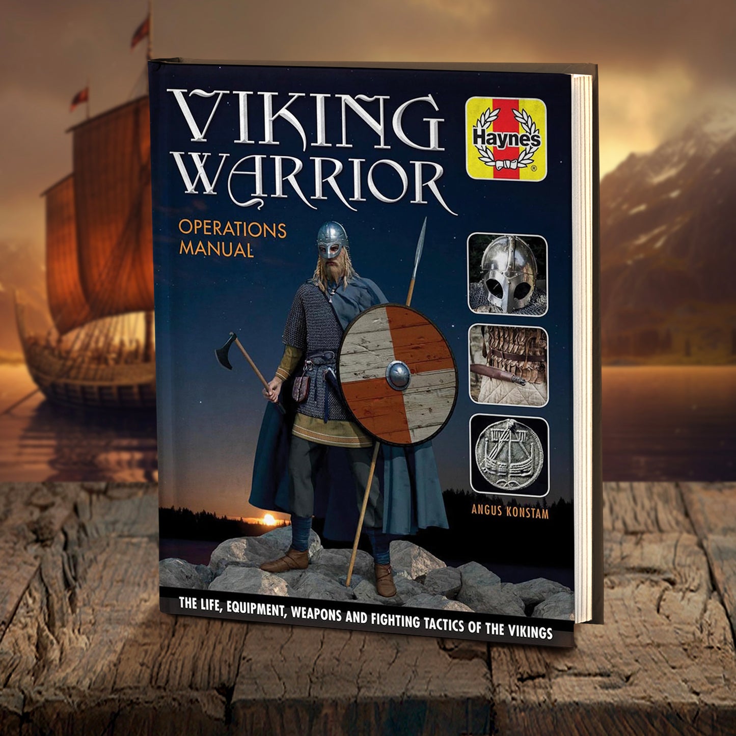 A hardcover book on a wooden table. The cover depicts a Viking warrior standing on a pile of rocks, wearing battle armor with a steel helmet and a blue cloak. He is carrying a round shield in one hand, and an axe in the other hand. In the background is a forest with the setting sun at the top. White text says "Viking warrior operations manual. The life, equipment, weapons and fighting tactics of the vikings." In the background is a Viking longship on the water, next to a mountain.