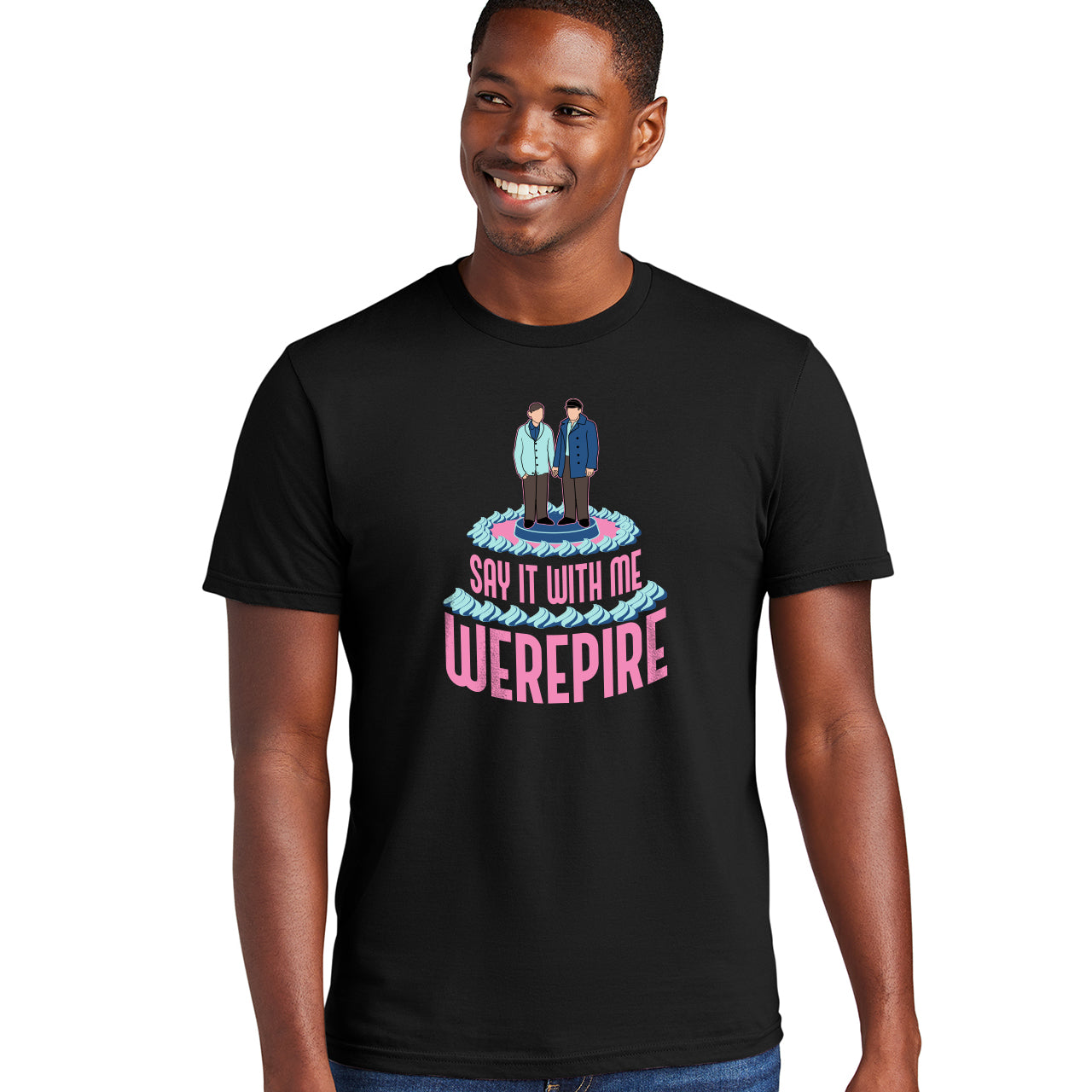 A male model wearing a black t-shirt, against a white background. On the front of the shirt is pink text that says "say it with me, werepire." Above the text is a depiction of a wedding cake topper with two grooms holding hands.