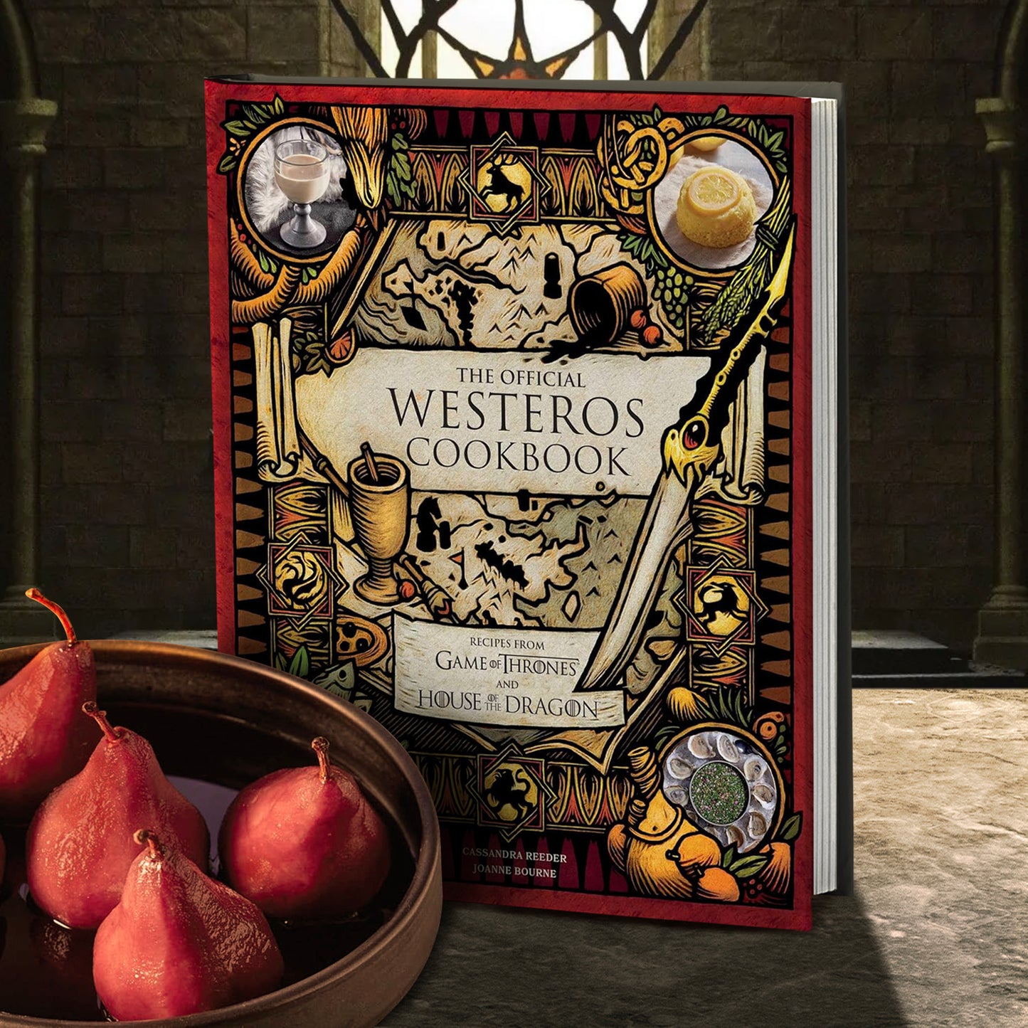 A hardcover cookbook on a stone table. The cover depicts a map of Westeros from the "Game of Thrones" series, with family sigils around the borders. In the corners are images of dishes from the cookbook. Black text says "The official Westeros cookbook. Recipes from Game of Thrones and House of the Dragon." In front of the book is a bowl with candied pears. In the background is a castle room.