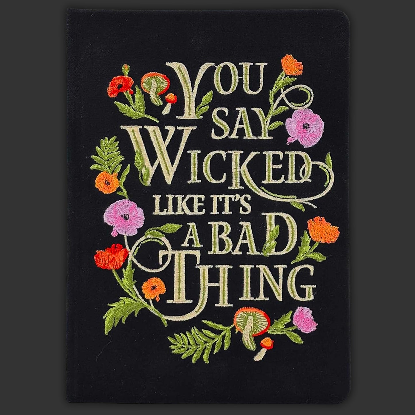 A black embroidered journal with flowers around the borders. White text says "you say wicked like it's a bad thing."