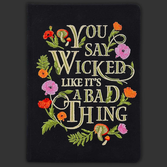 A black embroidered journal with flowers around the borders. White text says "you say wicked like it's a bad thing."