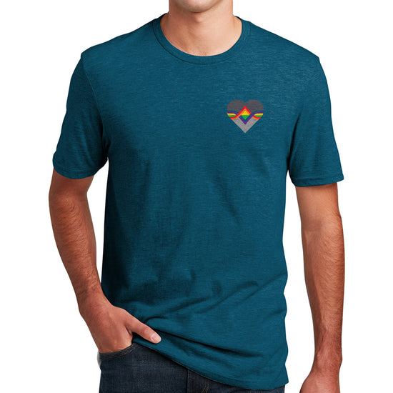 A male model wearing a teal T-shirt. The Acting Ensign Pride symbol is at the top left corner of the shirt. The symbol is a grey heart with rainbow lines running through the center.