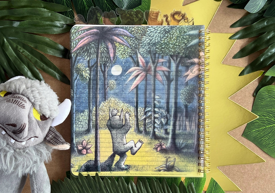 A page from the book showing Max in his wolf costume, in a dark forest. The journal is on a table surrounded by leaves and a goat puppet.