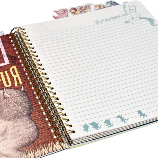 A blue journal depicting Max and two monsters from Where the Wild Things Are. Two monsters are carrying Max on their shoulders. At the top is a banner across two trees with text saying where the wild things are. At the top of the journal are tabs depicting characters from the book. On the left and bottom are red lines with the dimensions od the journal in red.