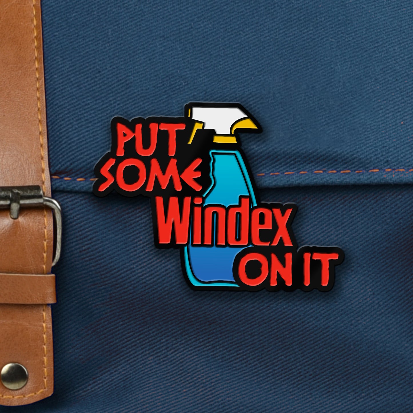 A pin depicting a blue spray bottle against a blue canvas bag. Red text across the pin says "Put some Windex on it."