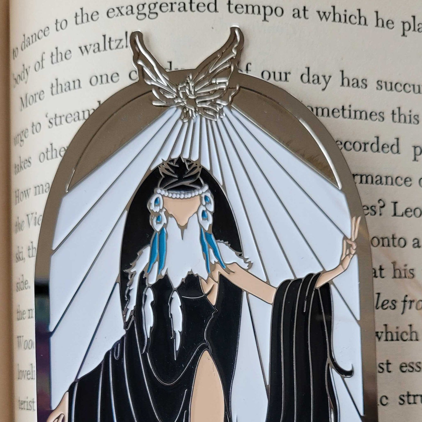 Close up view of a bookmark on the pages of a hardcover book. The bookmark depicts the ElfQuest character Winnowill, dressed in black robes with white rays above her