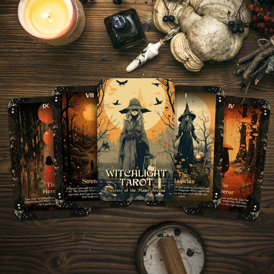 A collection of witch-themed tarot cards on a wood table. Each card has drawings related to witchcraft, along with descriptions of the major arcana each represents. Around the cards are candles, herbs, and other witchcraft items.