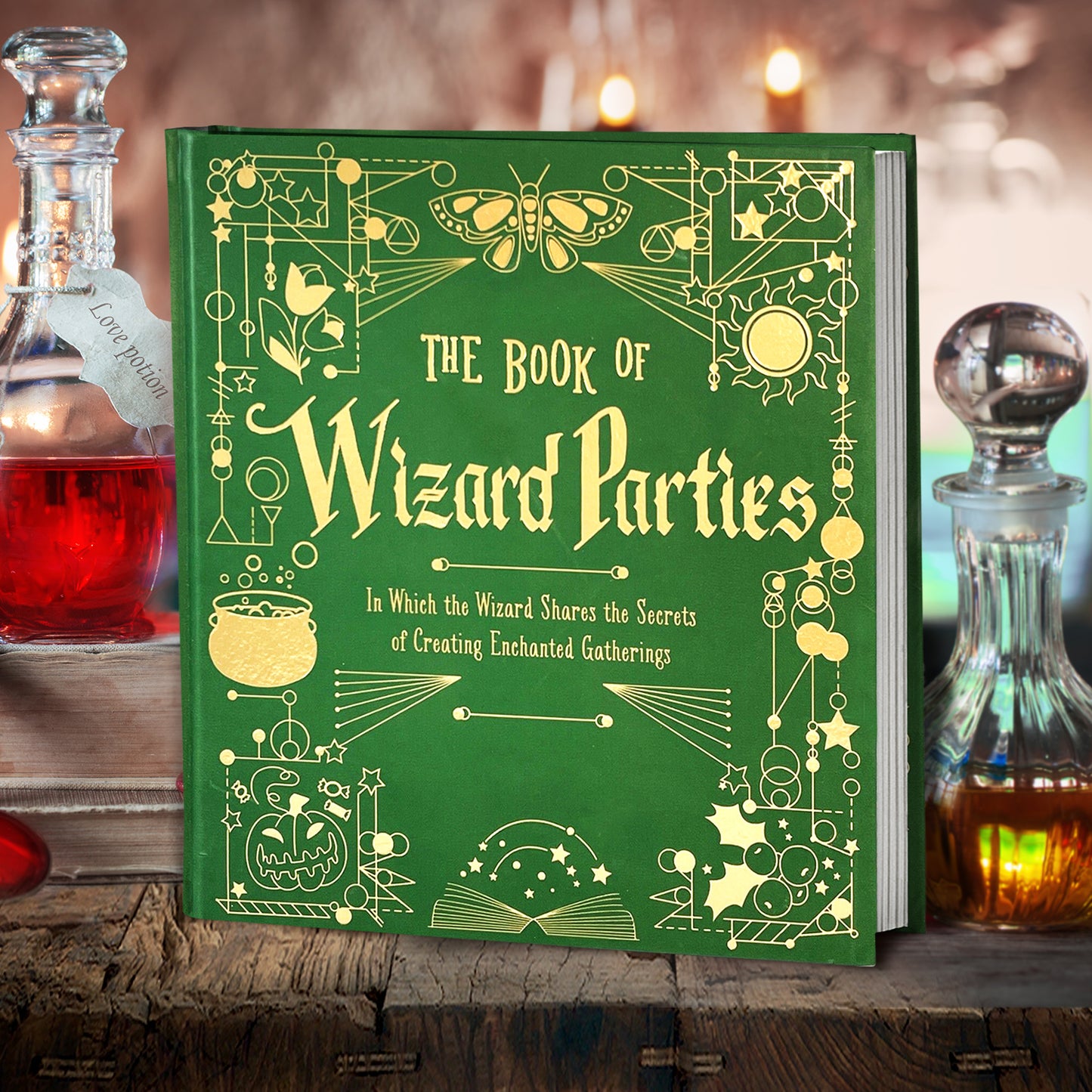 A green book on a wood table, next to crystal decanters filled with colorful potions. On the book's cover are yellow etchings of wizard and witch craft tools and spell ingredients. At the top in yellow text is "The Book of Wizard Parties: In Which the Wizard Shares the Secrets of Creating Enchanted Gatherings"