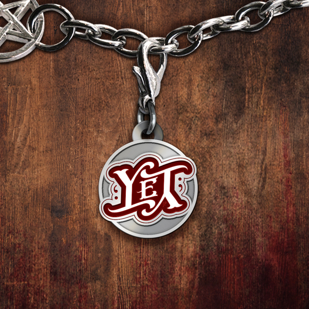 A silver-toned charm with a round charm featuring the word 'YET' in red and white script on a silver background, displayed against a dark wood surface.