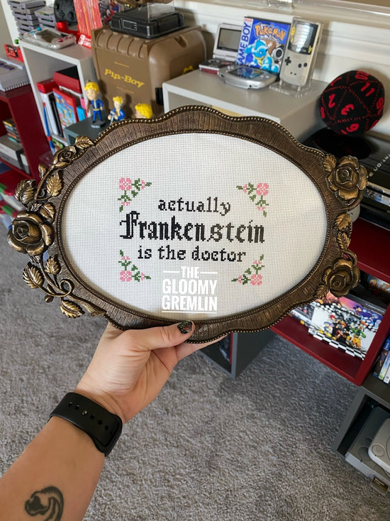 Decorative sign with text saying "Actually Frankenstein is the doctor" held by a model's hand. In the background are vintage toys and games.