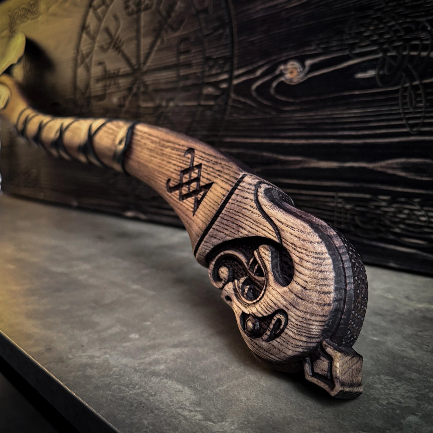Close up of the hilt of a wooden axe handle. Behind the axe is a wooden case with a Viking compass design on the top.