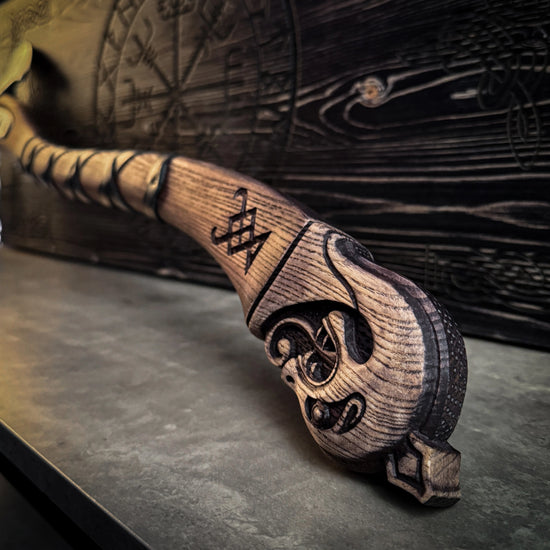 Close up of the hilt of a wooden axe handle. Behind the axe is a wooden case with a Viking compass design on the top.