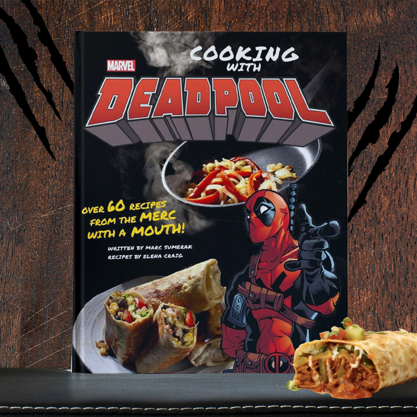 A book with "Cooking with Deadpool" as the title, "over 60 recipes from the merc with a mouth" and " written by Marc Sumerak, recipes by Elena Craig” on the front with various dishes with food. Deadpool drawn like his comic book format is pointing to camera. The book is on a leather shelf next to a chimichanga and behind the book is a wooden wall with Wolverine claw marks.