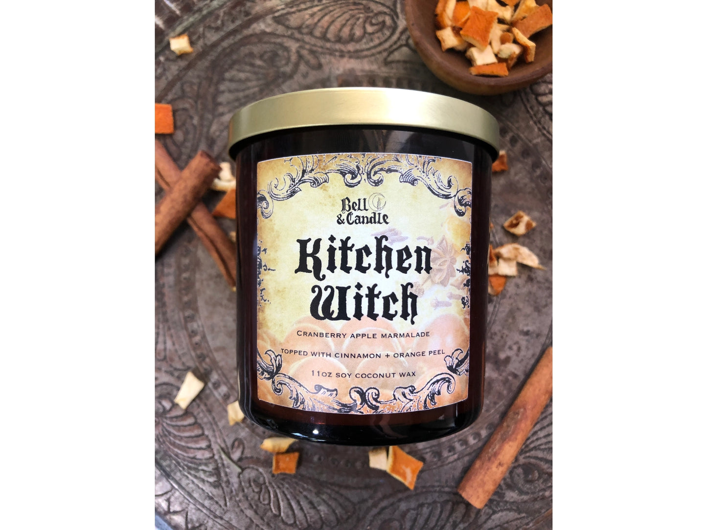 Bell & Candle 'Kitchen Witch' candle with decorative label on a textured surface.