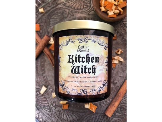 Bell & Candle 'Kitchen Witch' candle with decorative label on a textured surface.