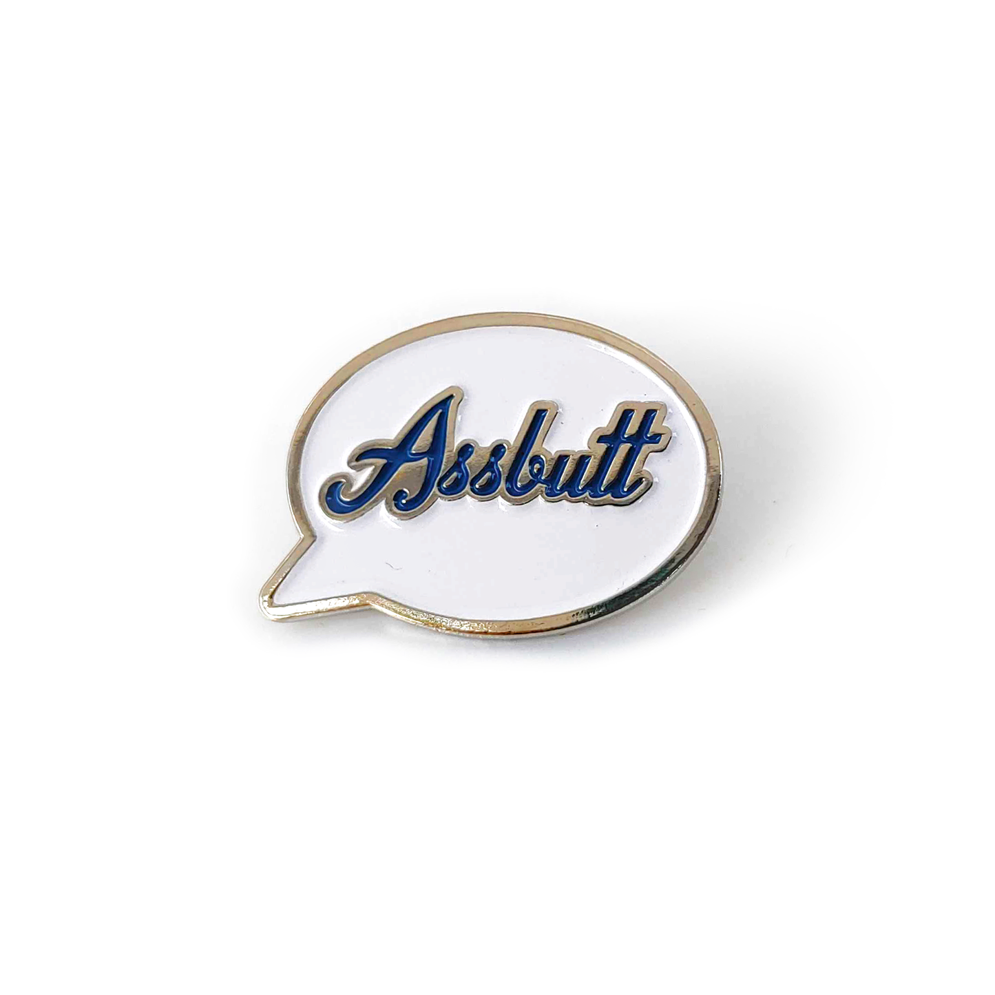 A silver pin with a white front in the shape of a speech bubble. The word "Assbutt" is written in blue script font.