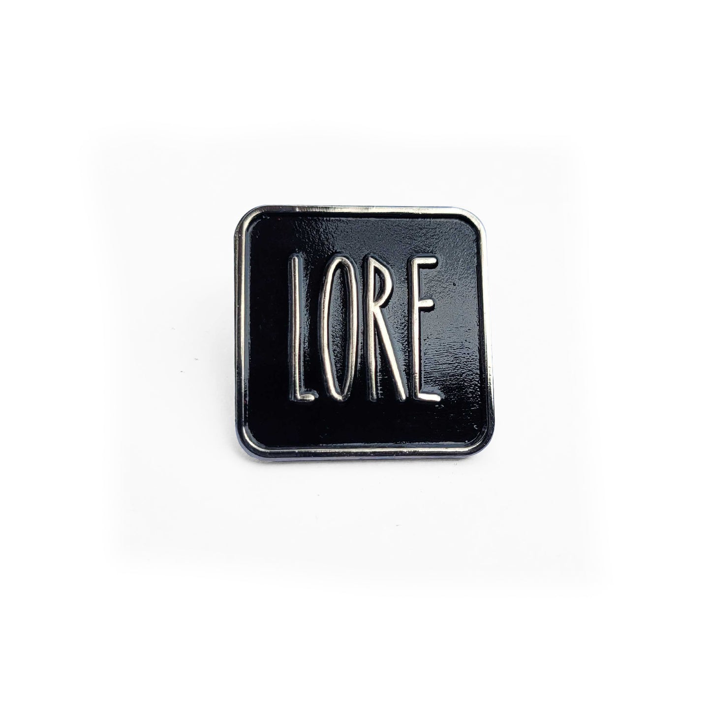 A silver enamel pin with a black rectangular front, which reads LORE in tall, skinny white font