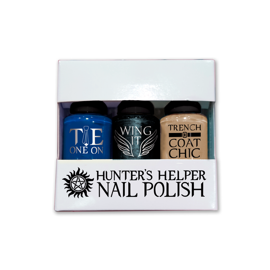 A white, windowed box with the words "Hunter's Helper Nail Polish" and an anti-possession symbol in black. There are 3 cylindrical bottles of nail polish in the box labeled "Tie One On (indigo blue) "Wing It" (a  shimmering gray), and "Trench Coat Chic" (a tan color).