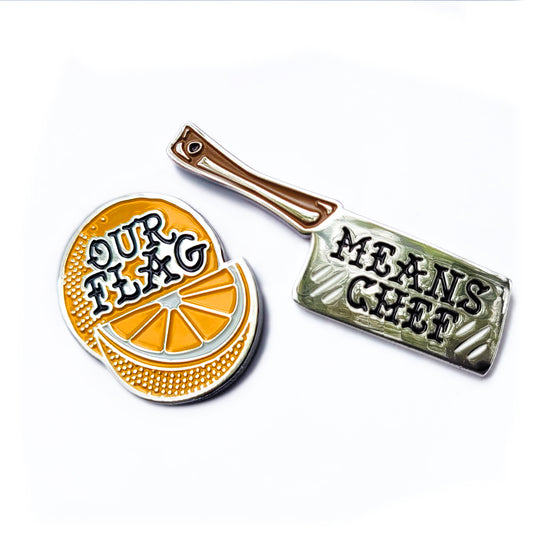 Load image into Gallery viewer, A set of two colored enamel pins: an orange slice with &amp;quot;our flag&amp;quot; in writing and a meat cleaver with &amp;quot;means chef&amp;quot; in writing.
