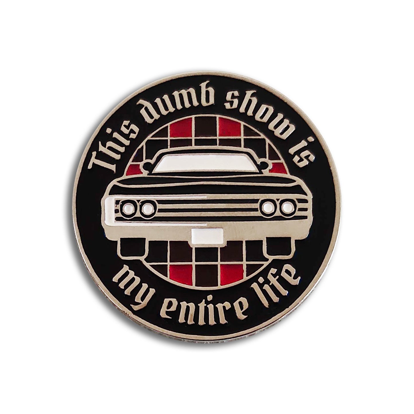 A circular black enamel pin that reads "THIS DUMB SHOW IS MY ENTIRE LIFE" around the edge. The center of the circle has a red-and-black checkered pattern and a vintage black Impala as seen from the front.